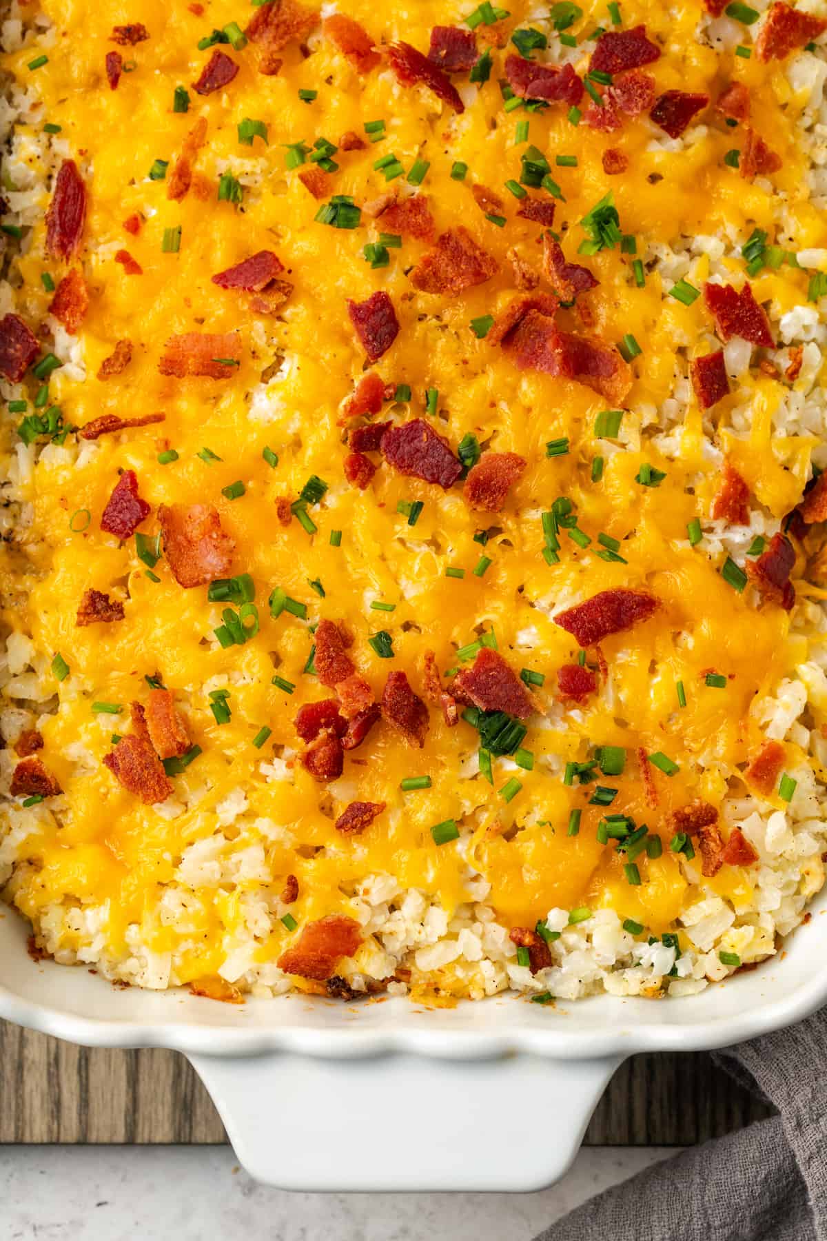 A cheesy cauliflower rice casserole topped with bacon and chives after being baked.