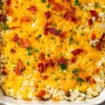 A baked cheesy cauliflower rice casserole in a white dish with bacon and green chives sprinkled on top and a text overlay on the photo.