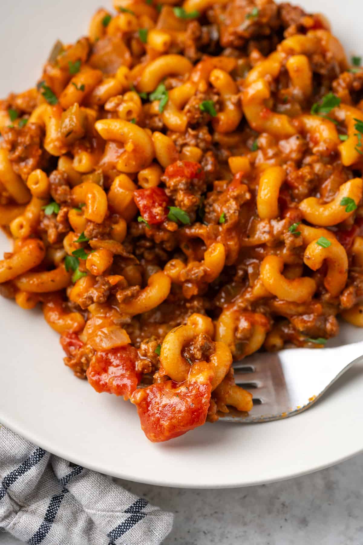 A fork scooping up a bite of goulash from a white round plate.