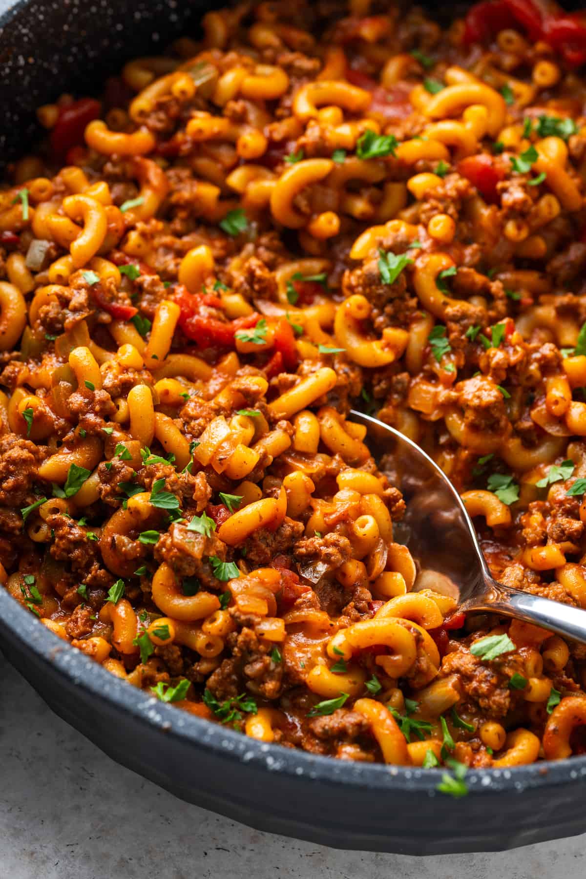 A spoon scooping up some goulash from a large skillet.