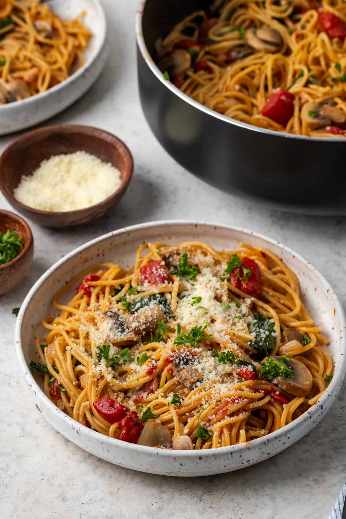 Vegetarian spaghetti served in a low bowl with parsley and Parmesan on top and the one pot pasta skillet in the background.