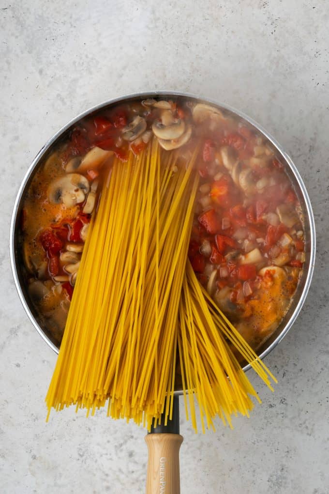 Spaghetti noodles being added to a one pot pasta mixture in a skillet.