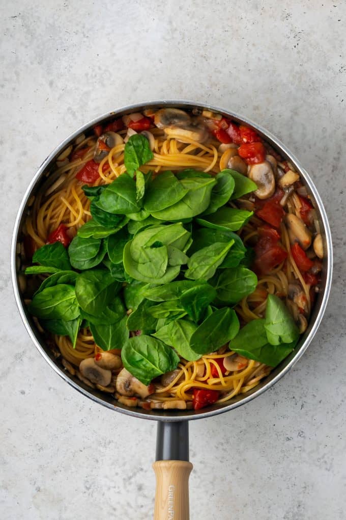 Fresh baby spinach added to a skillet of one pot vegetarian spaghetti.