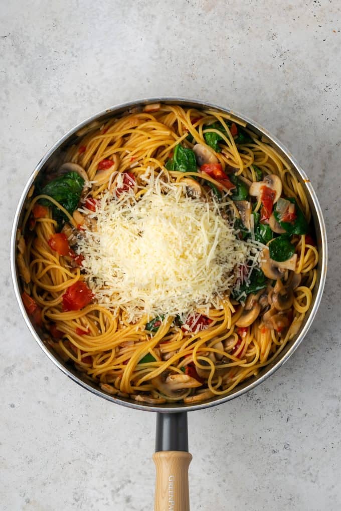 Grated Parmesan cheese added to a one pot vegetarian spaghetti dish in a large skillet.