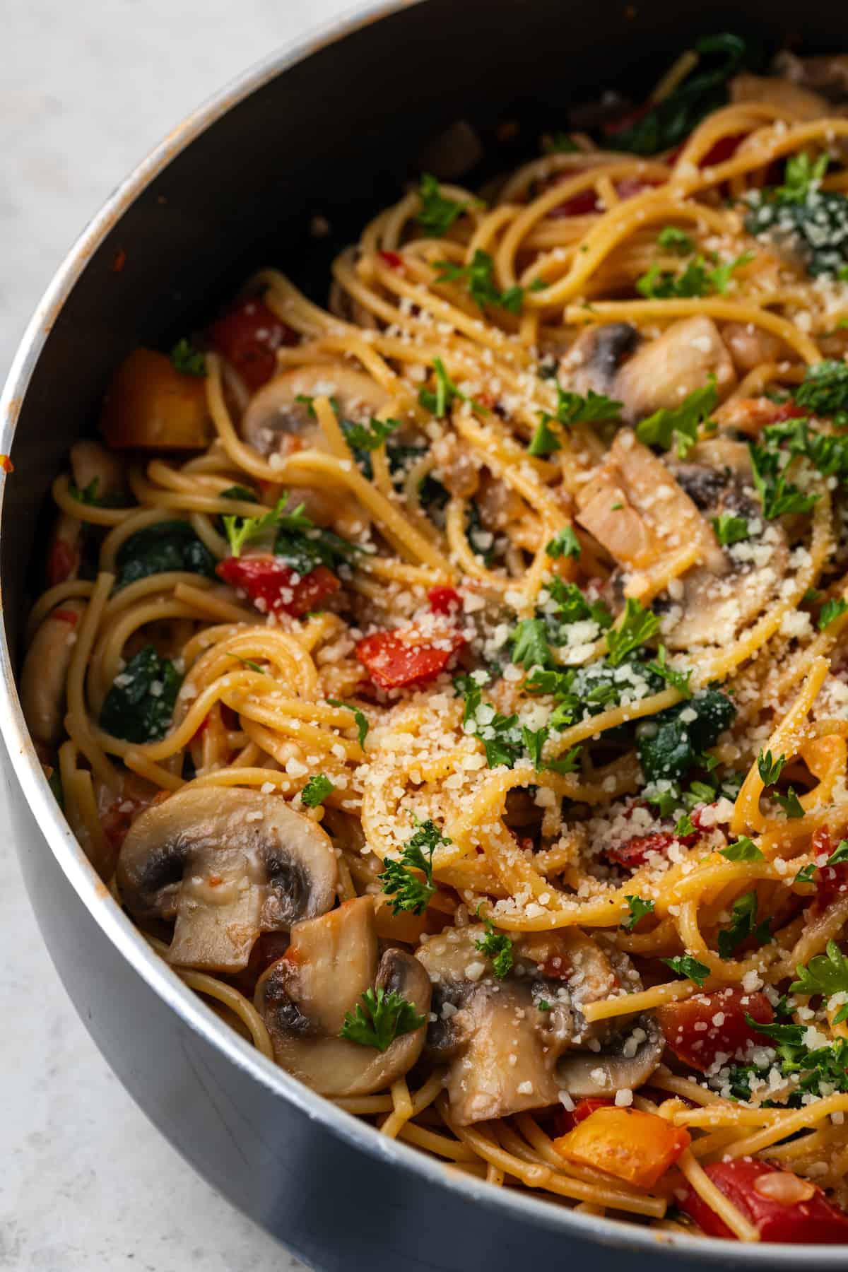 Close up of vegetarian spaghetti with mushrooms, spinach and tomatoes all cooked in a large skillet.