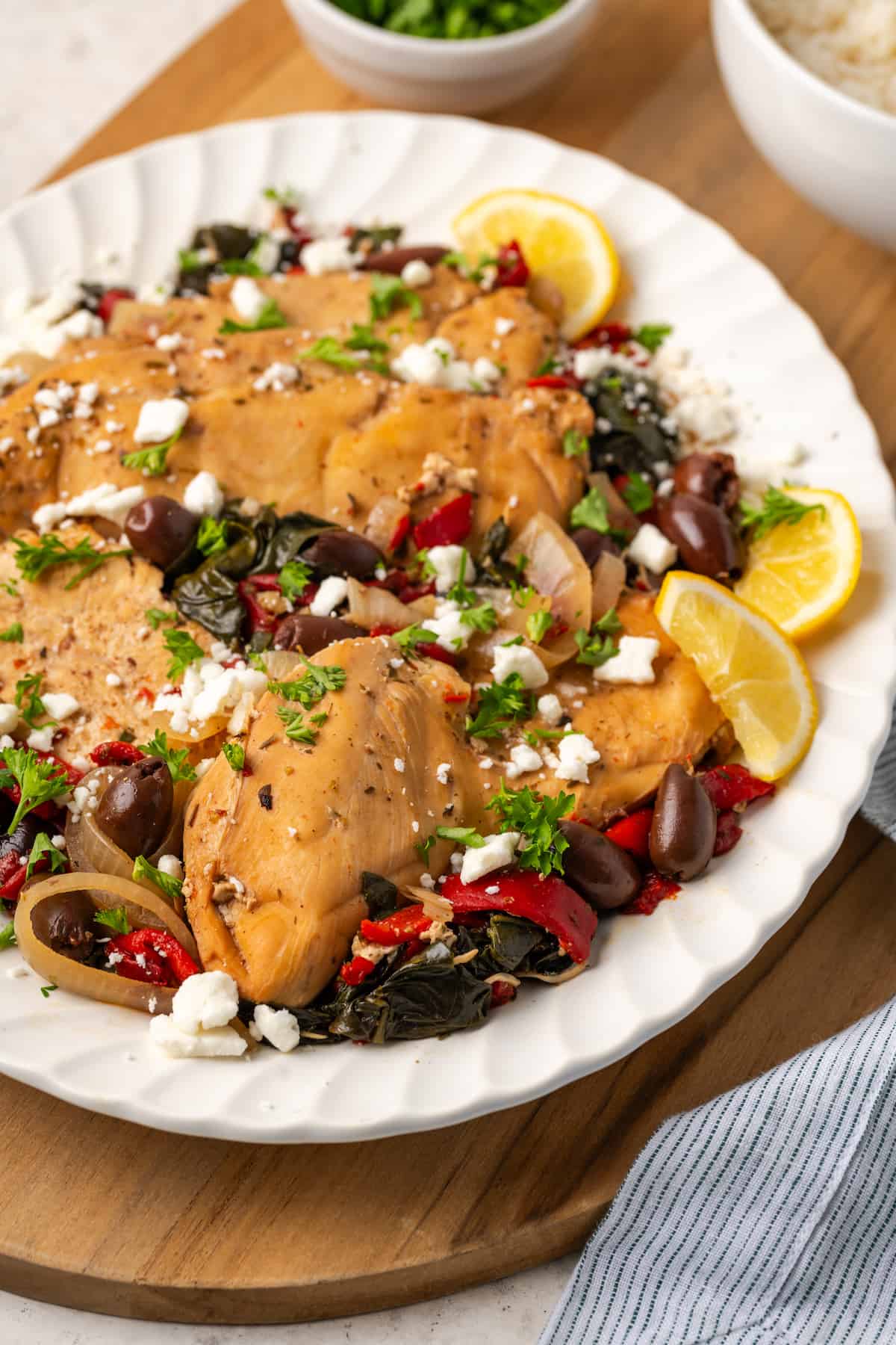 A slow cooker Greek chicken dinner served on a white platter with lemon slices for garnish.