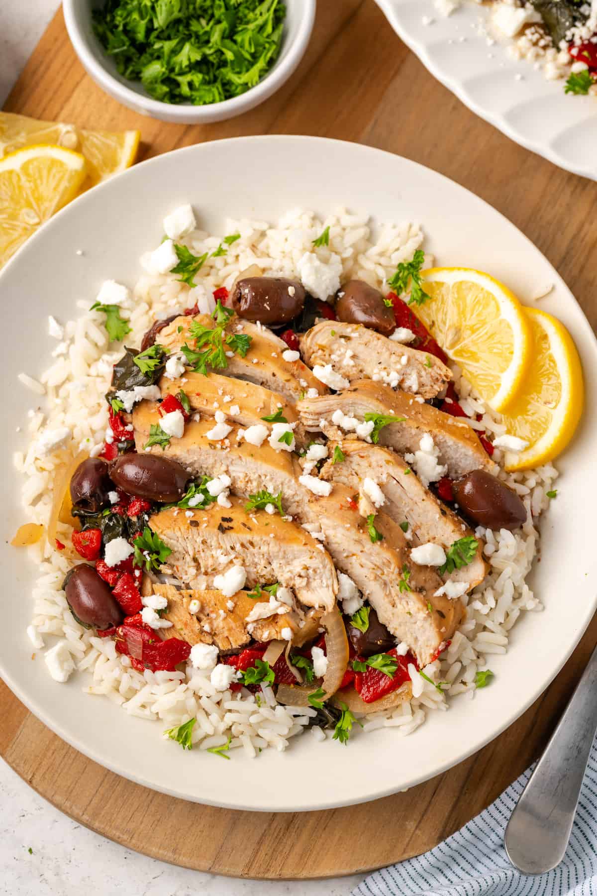 Sliced chicken with roasted red peppers, olives and spinach served over steamed rice on a dinner plate.