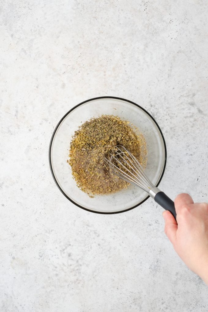 A whisk mixing together herbs and vinegar in a small glass bowl.