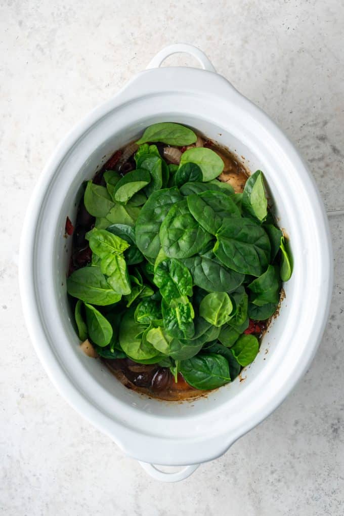 Fresh baby spinach being added to a slow cooker.