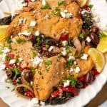 A white platter with slow cooker Greek chicken with olives, peppers and onions topped with feta cheese and fresh herbs with a text overlay on the photo.
