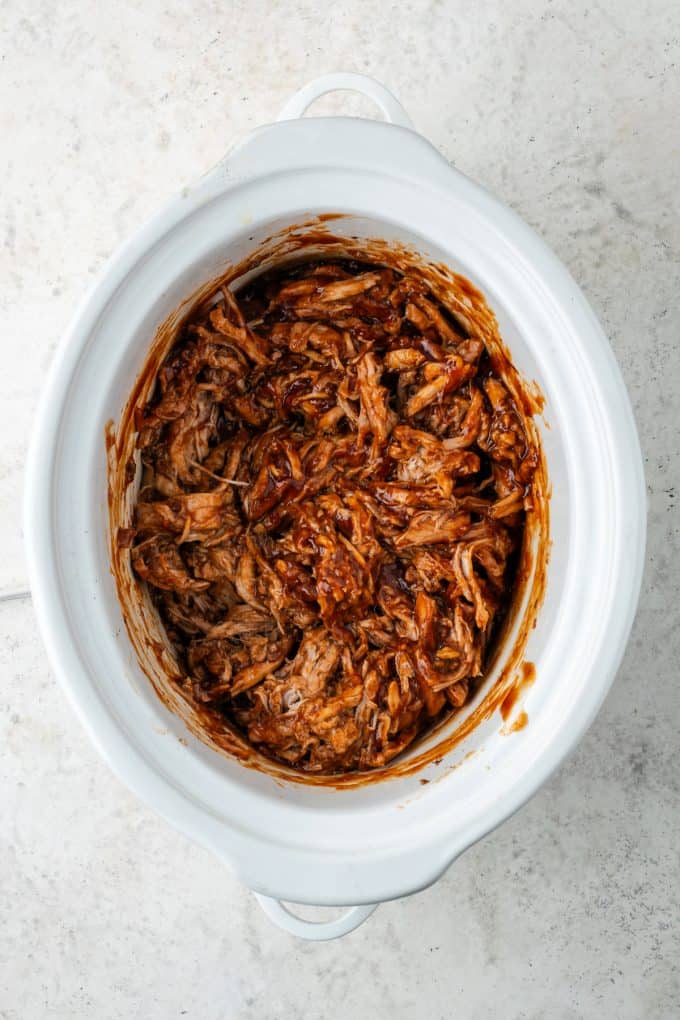 BBQ sauced pulled pork in a white slow cooker.