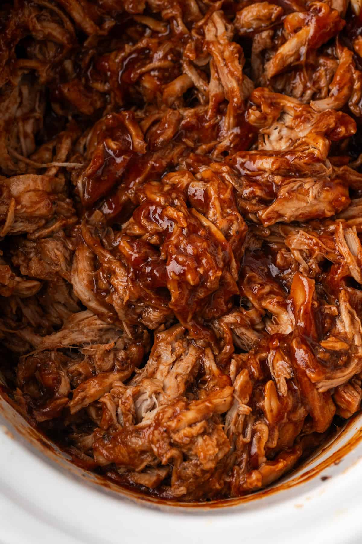 Close up of pulled pork with BBQ sauce in a slow cooker insert.