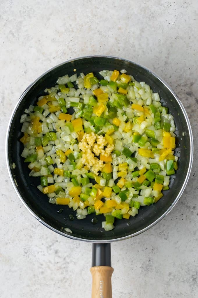 A skillet with sautéed onion and peppers and garlic added in.