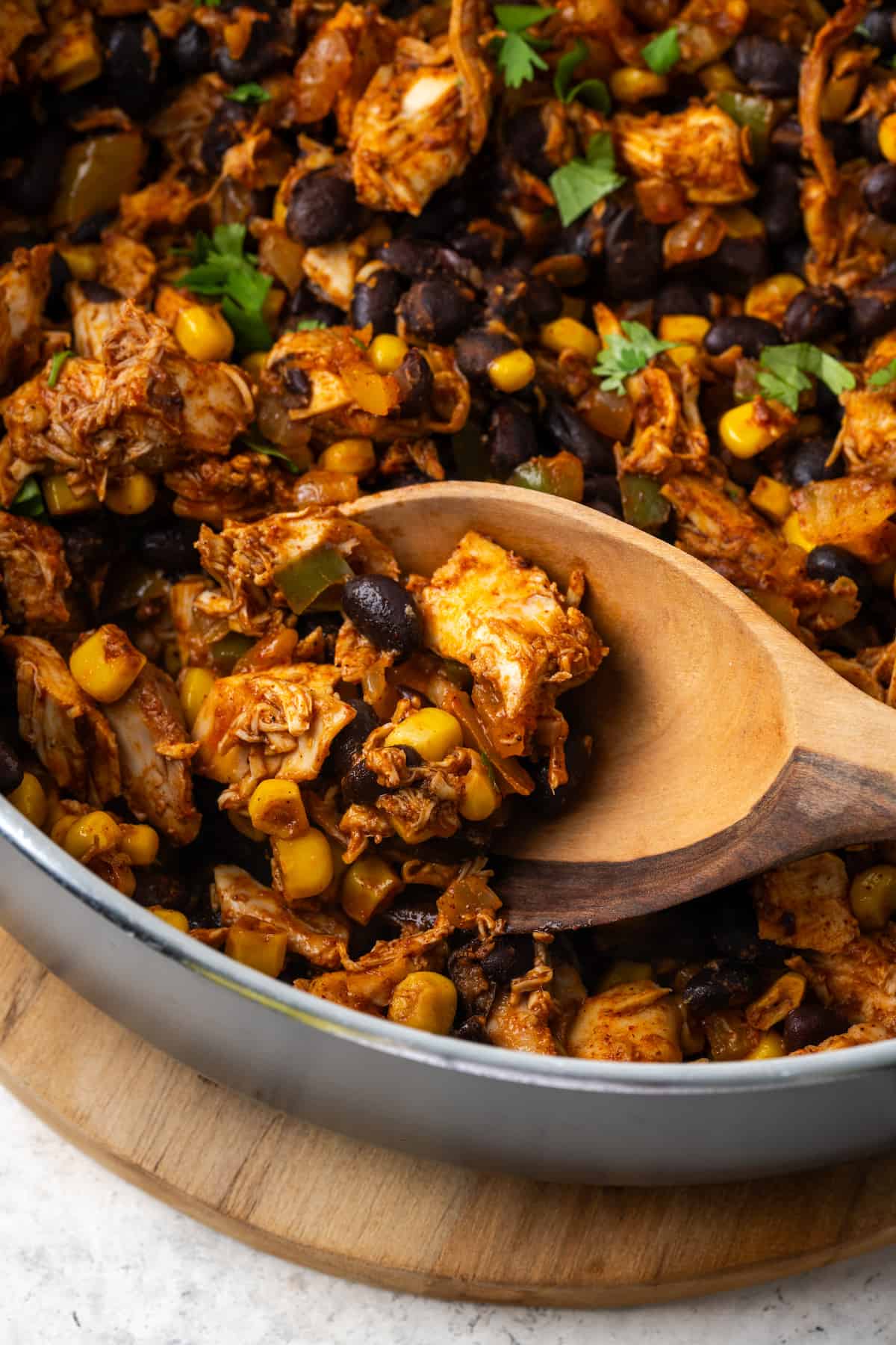 A wooden spoon lifting up a scoop of a southwest chicken mixture from a large skillet.