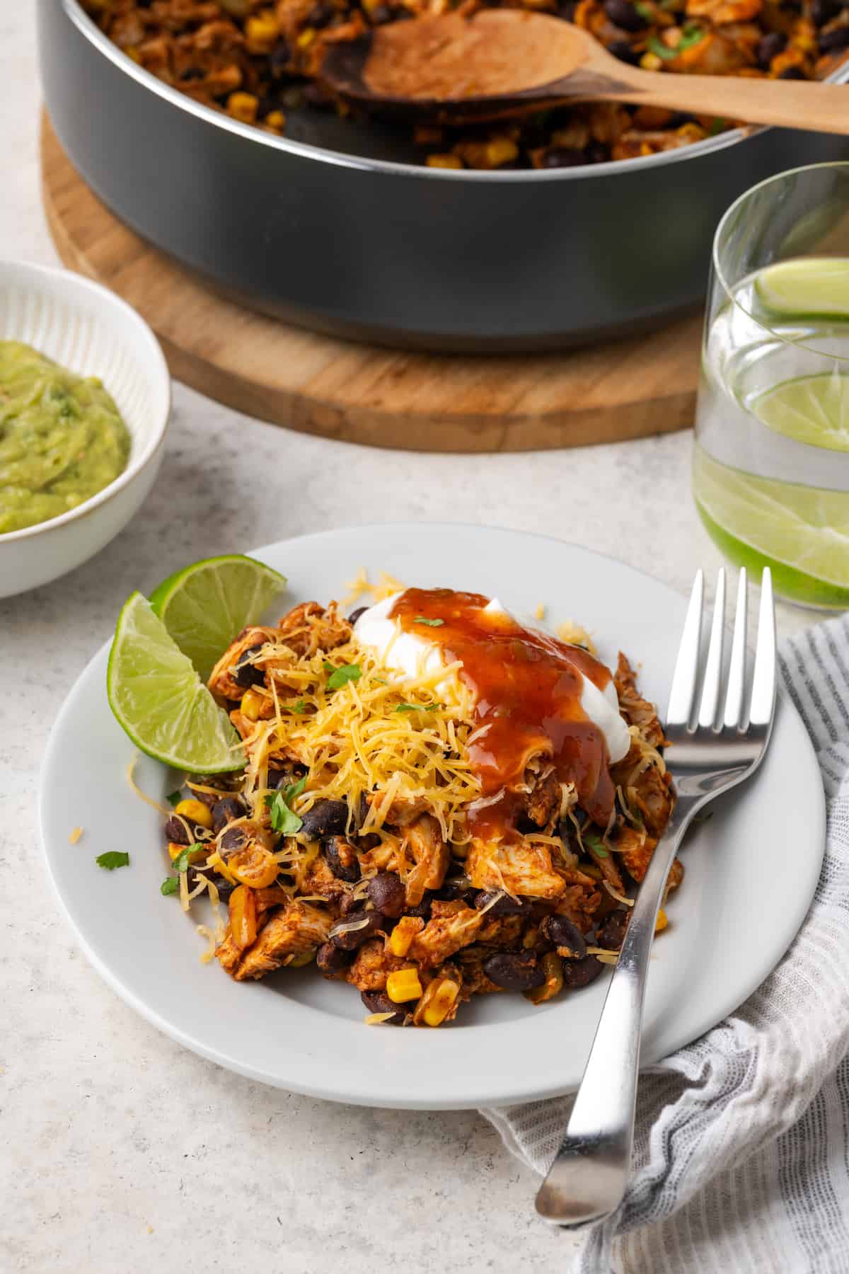 A serving of a southwest chicken and black bean mixture on a white plat with cheese, sour cream and salsa on top and a fork to the side.