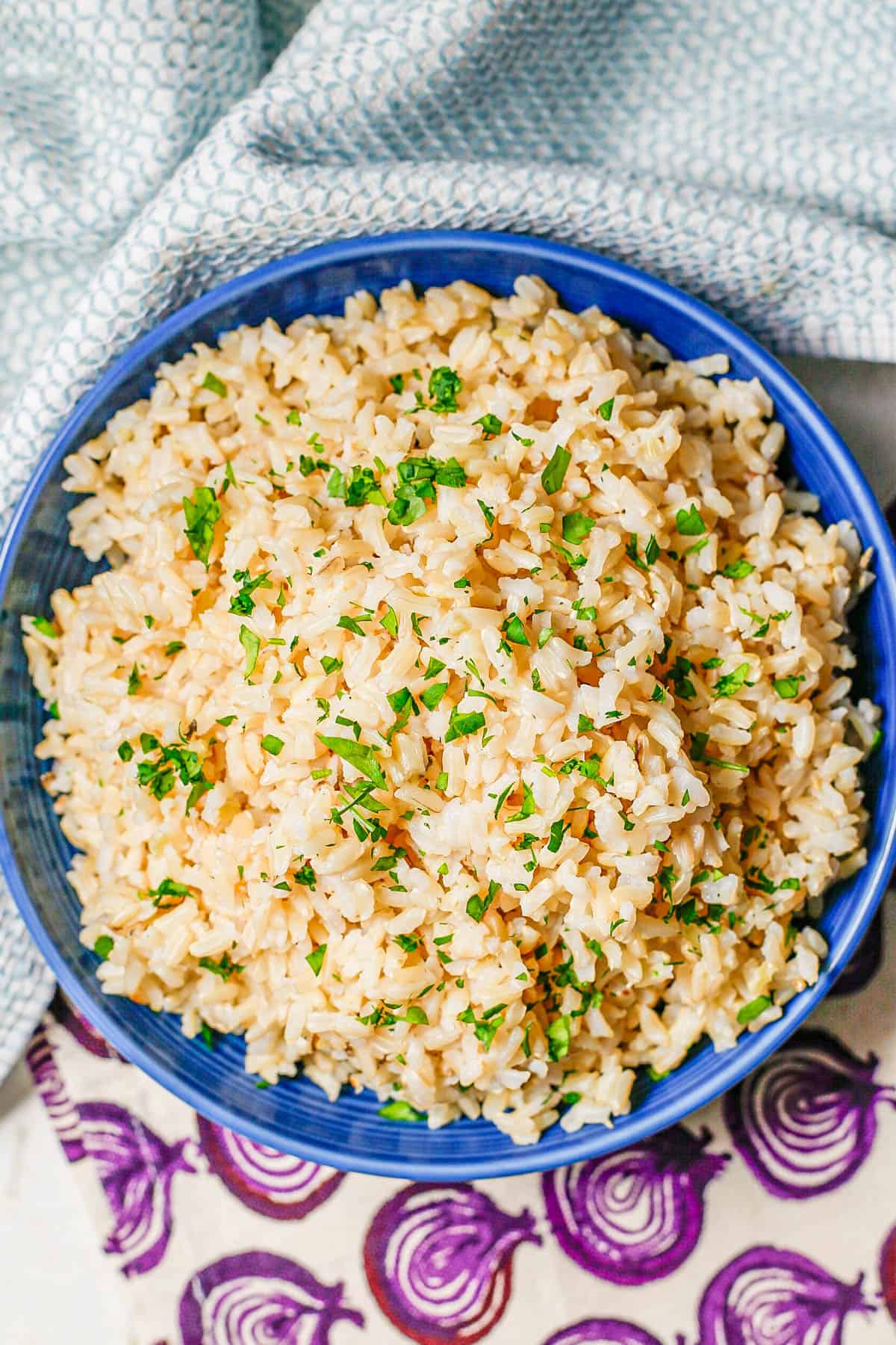 Fluffy steamed brown rice in a blue bowl with chopped fresh parsley on top.