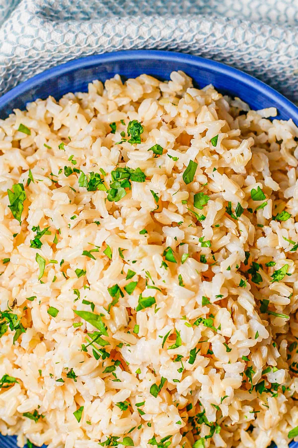 Close up of fluffy steamed brown rice in a blue bowl with chopped fresh parsley on top.