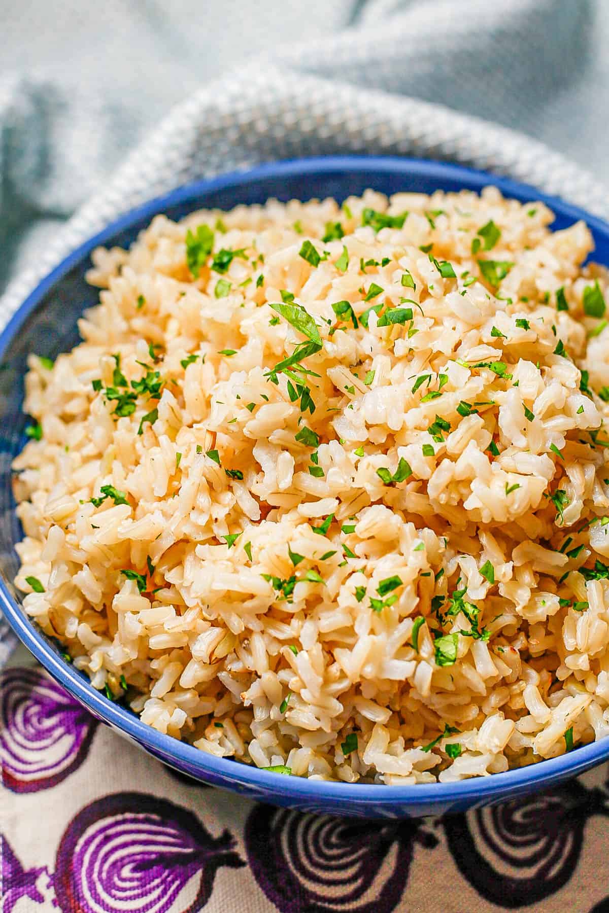 Close up of a blue bowl of steamed brown rice with parsley on top.