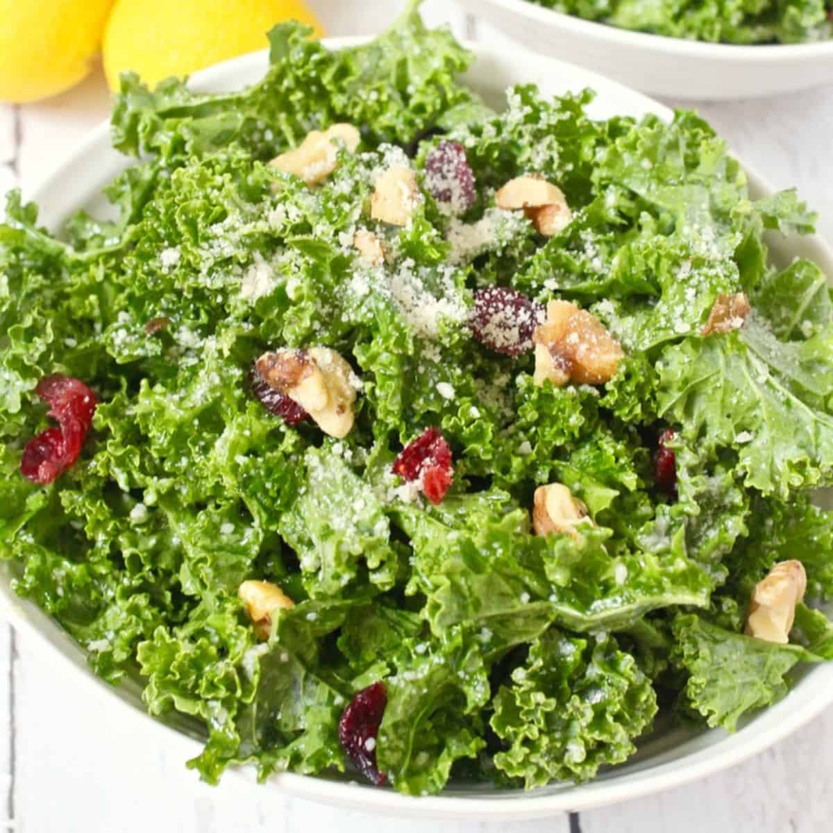Close up of a massaged raw citrus kale salad with walnuts, dried cranberries and Parmesan cheese.