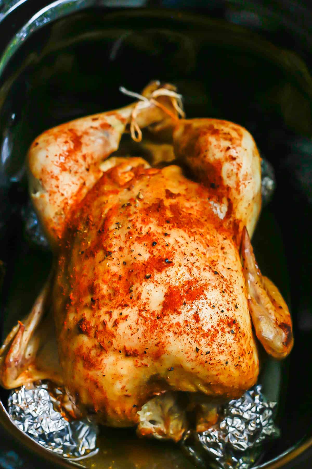 A seasoned and whole roasted chicken in a slow cooker insert.