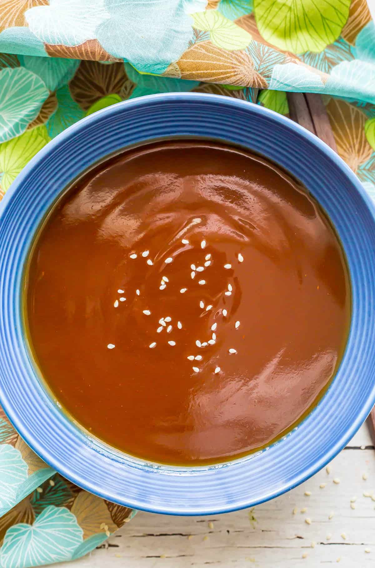 A blue bowl with a homemade sweet and sour sauce sprinkled with sesame seeds.