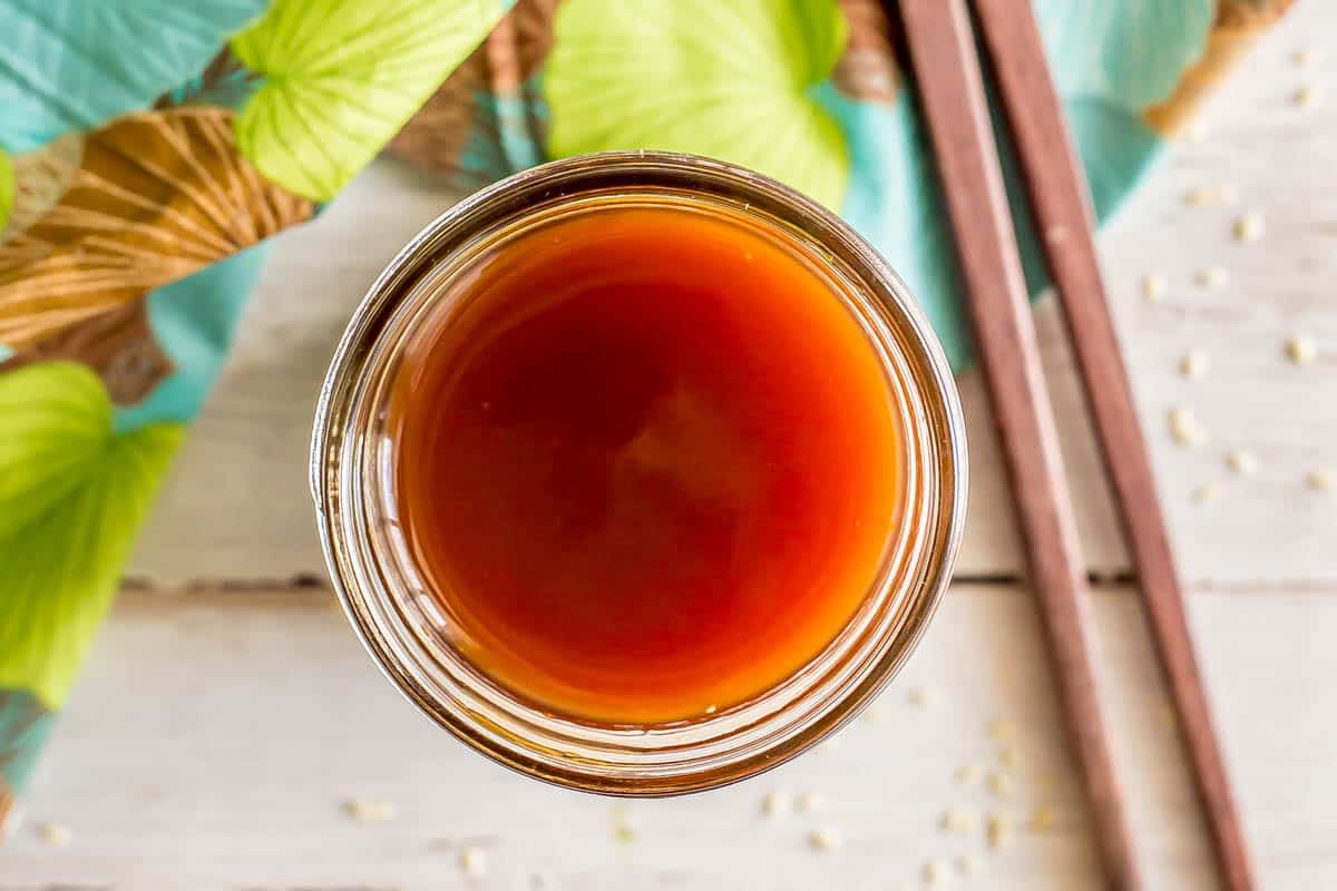 A brownish red Asian cooking sauce in a glass jar alongside some chopsticks.