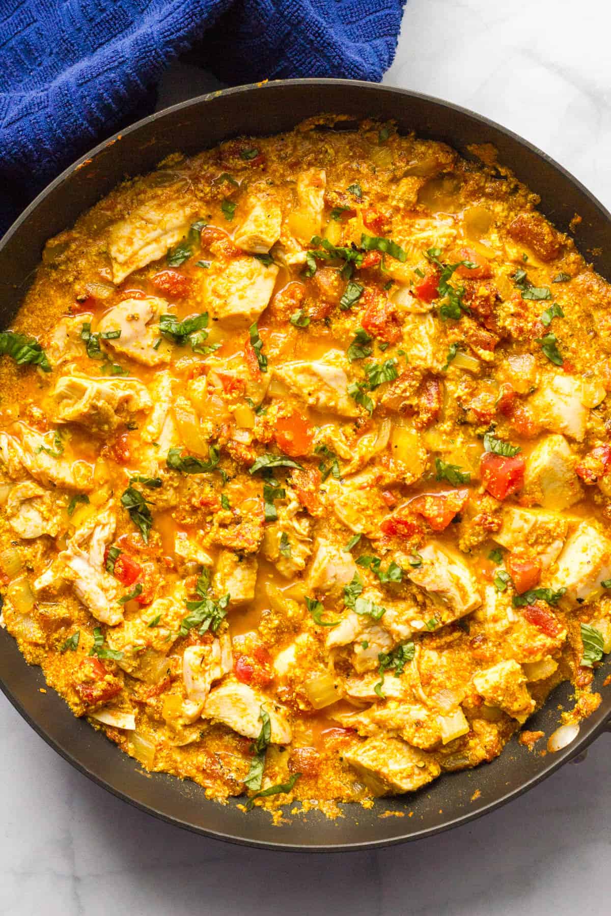 A large skillet with a quick and easy homemade chicken curry topped with chopped cilantro.