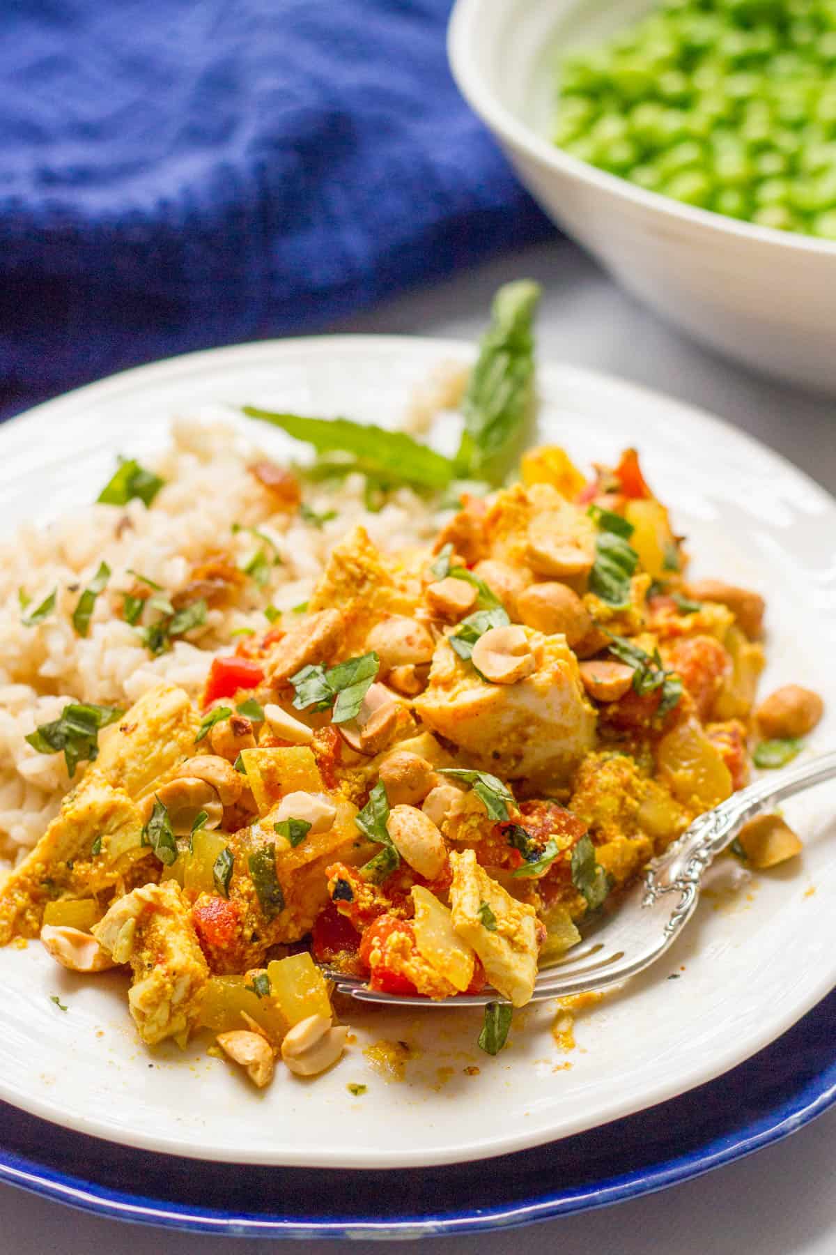 A fork resting on a white plate of steamed rice with chicken curry topped with cilantro and peanuts.