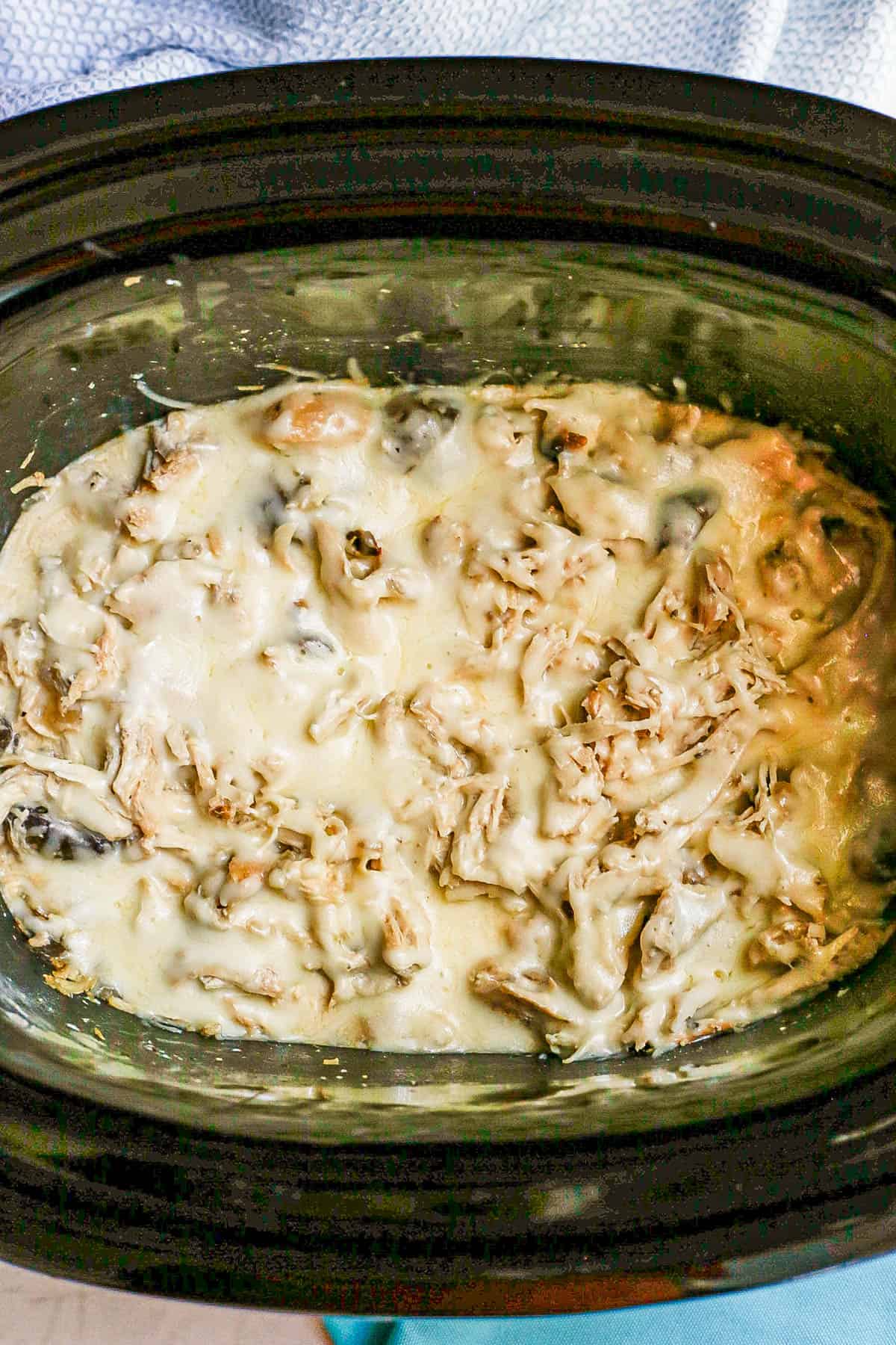 Shredded cheesy cream cheese chicken in a slow cooker insert.
