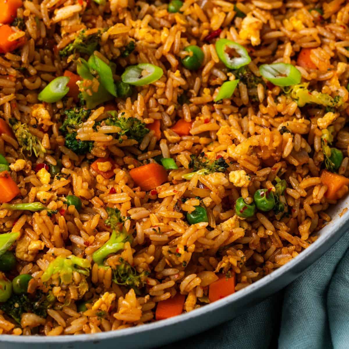 Close up of veggie fried rice with peas, carrots, broccoli and eggs in a large skillet.