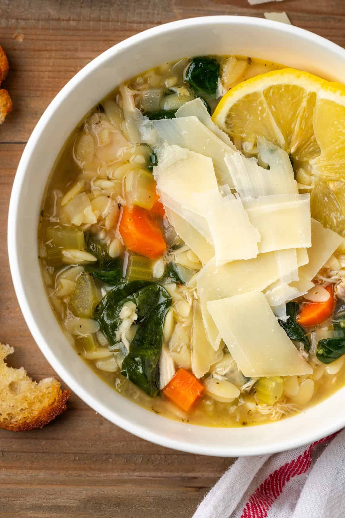 A bowl of lemony chicken orzo soup with fresh Parmesan on top and lemon slices to the side.