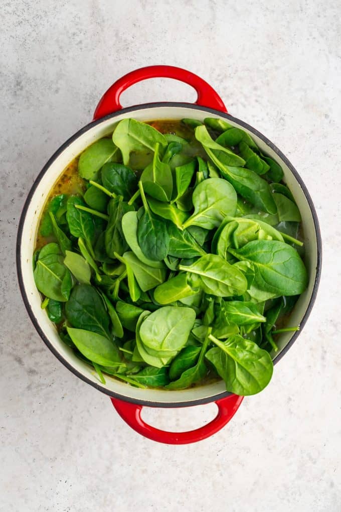 Fresh baby spinach being added to a soup in a large red pot.