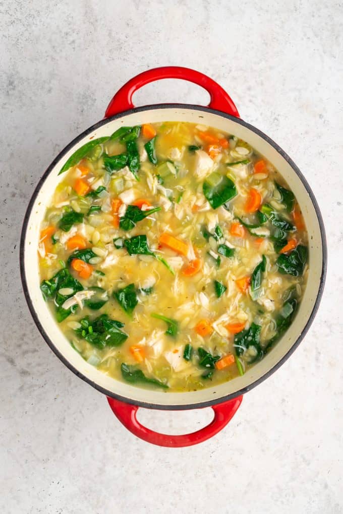 Chicken orzo soup with spinach being cooked in a large red pot.