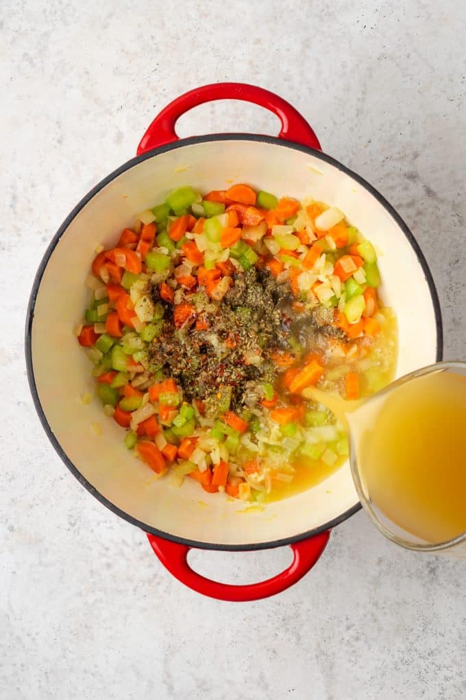 Broth being poured over a veggie and seasoning mixture in a large pot.