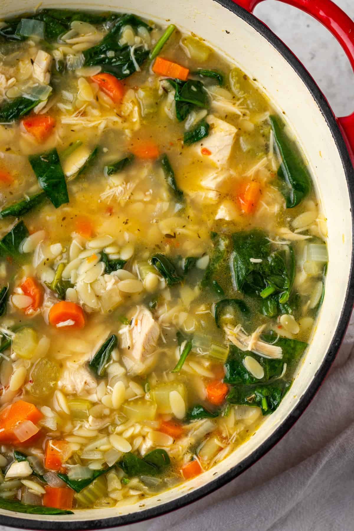 Chicken soup with orzo pasta, spinach and carrots in a large red soup pot.
