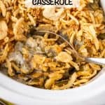 A silver serving spoon resting in a white crock pot of a classic green bean casserole with a text overlay on the photo.