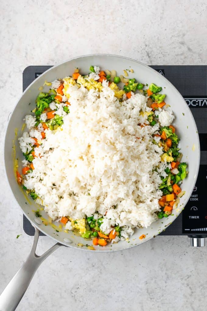 Steamed white rice being added to a skillet of mixed veggies and cooked eggs.