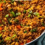 Close up of vegetable fried rice with peas, carrots, broccoli and eggs in a large skillet with a text overlay on the photo.