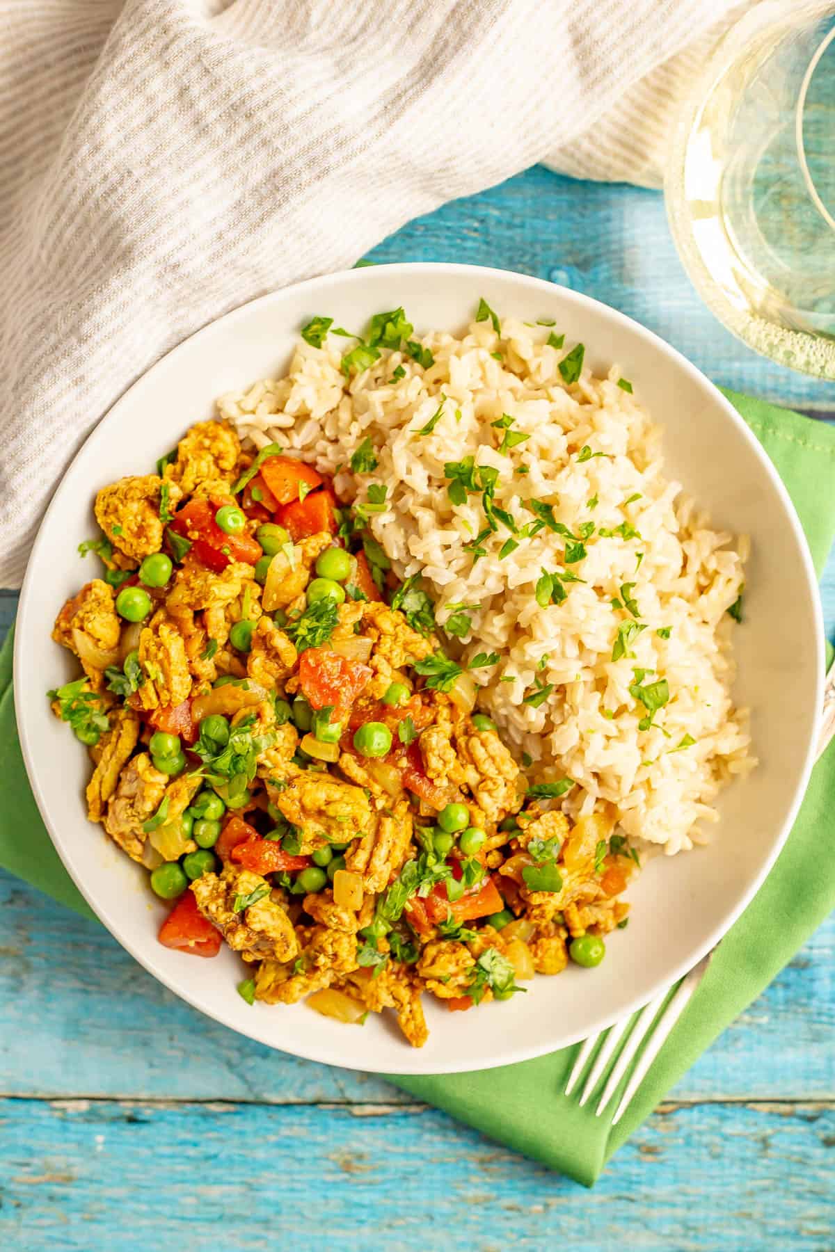 A low white bowl with rice alongside a ground turkey, tomato and pea mixture.