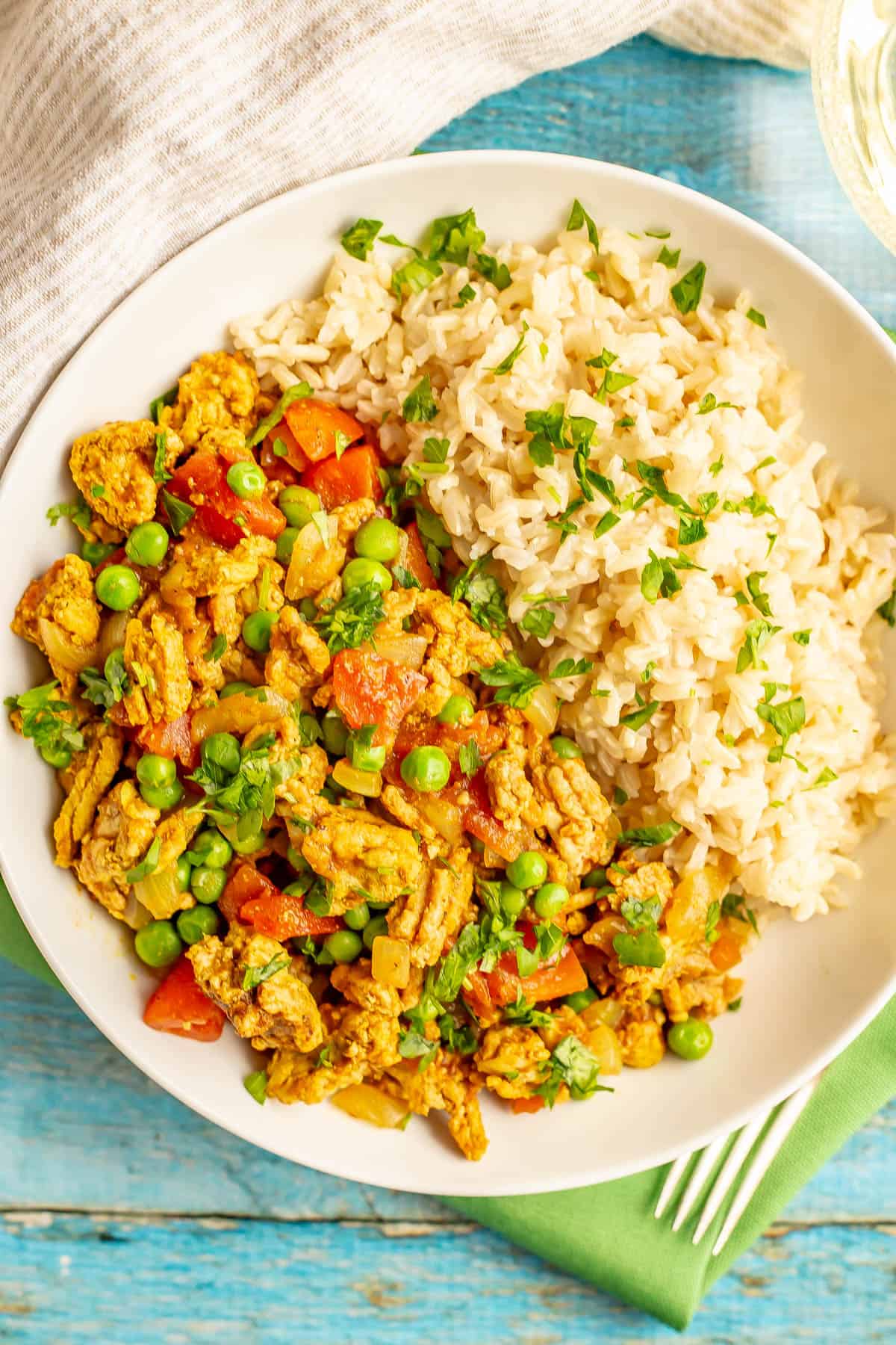 Close up of curry ground turkey with peas and tomatoes served alongside steamed rice in a low white bowl.