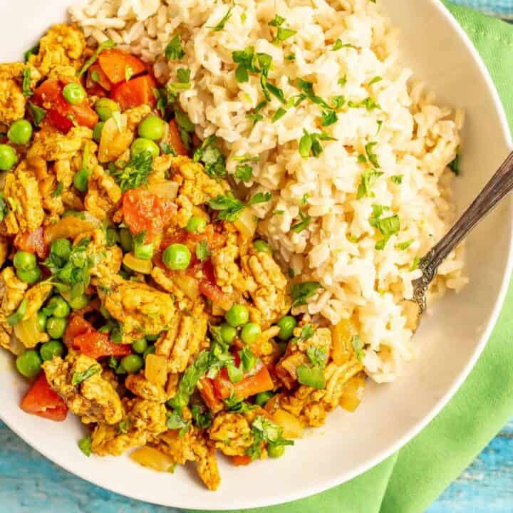 Close up of a fork resting in a bowl of rice and curried ground turkey with peas.