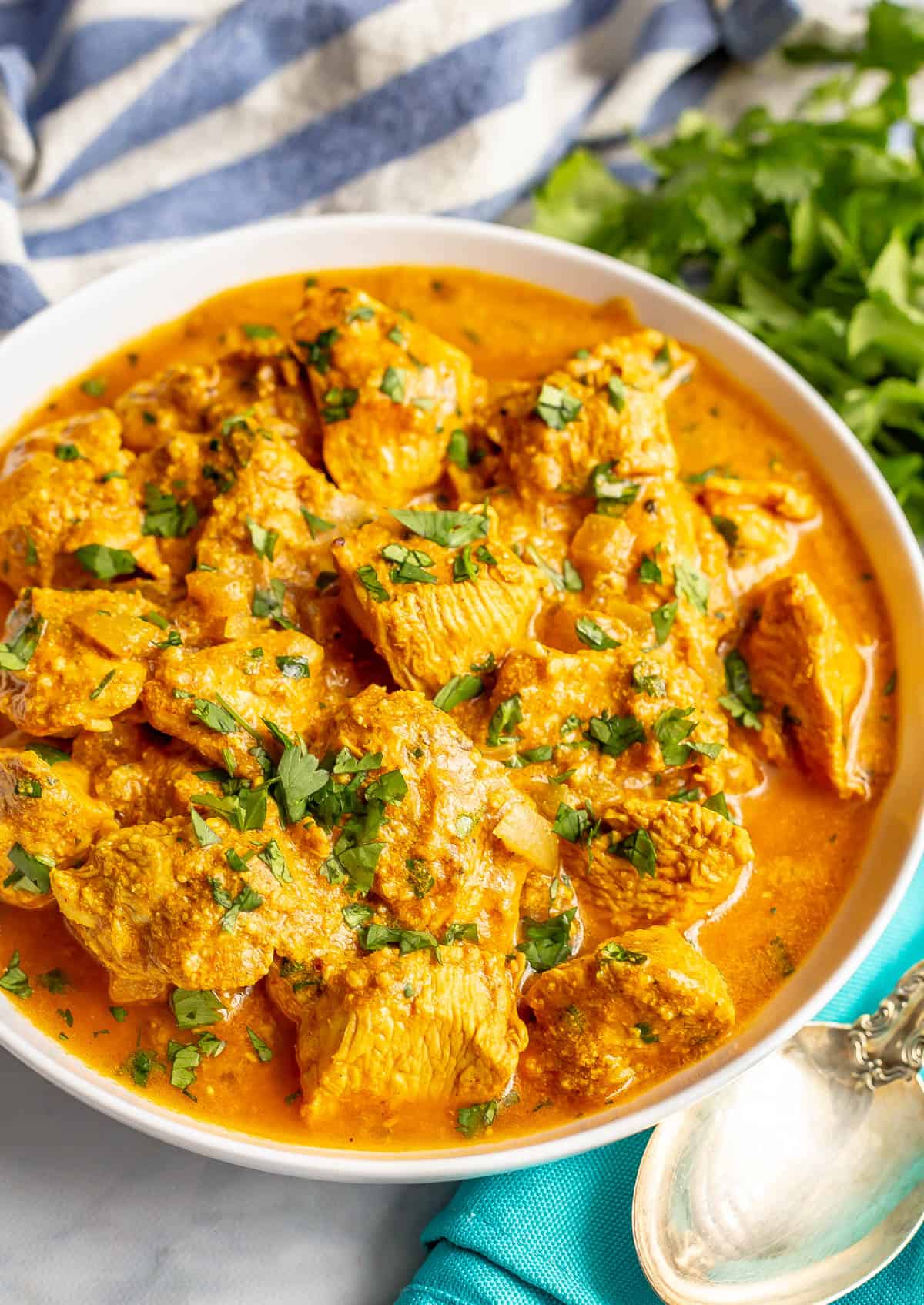 A large white serving bowl filled with an easy homemade butter chicken with sauce and a silver spoon resting to the side.