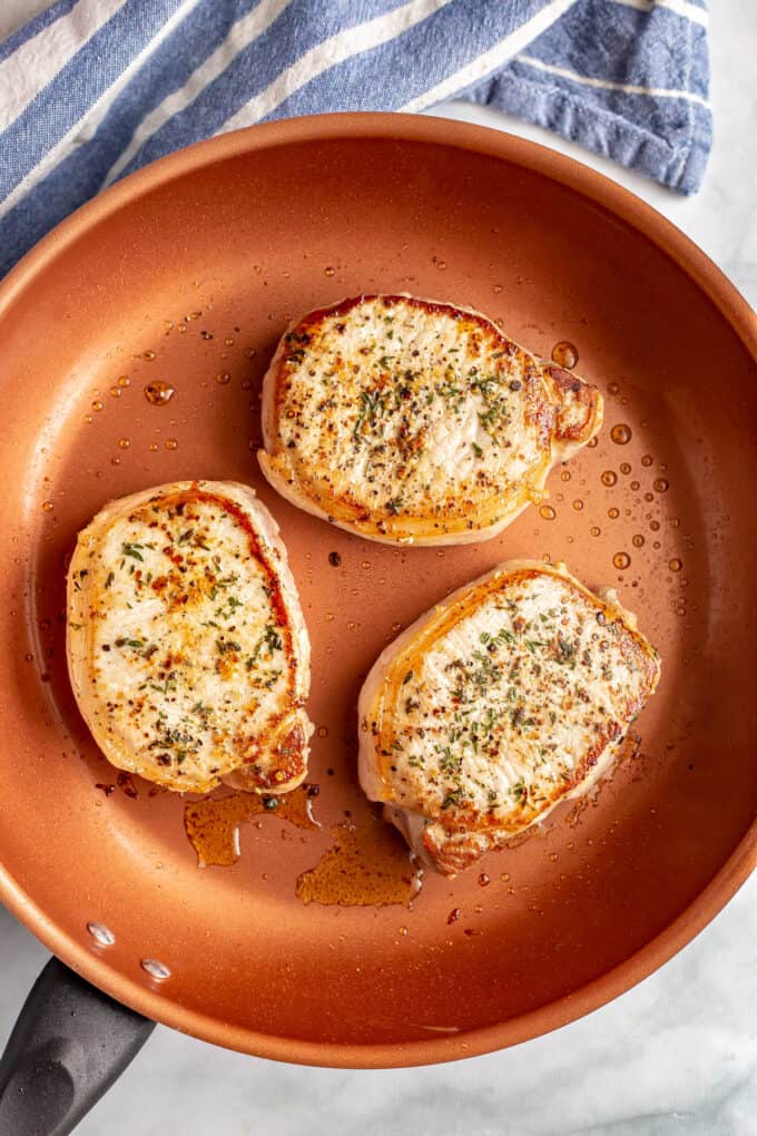 Three seared and browned pork chops in a large copper skillet.