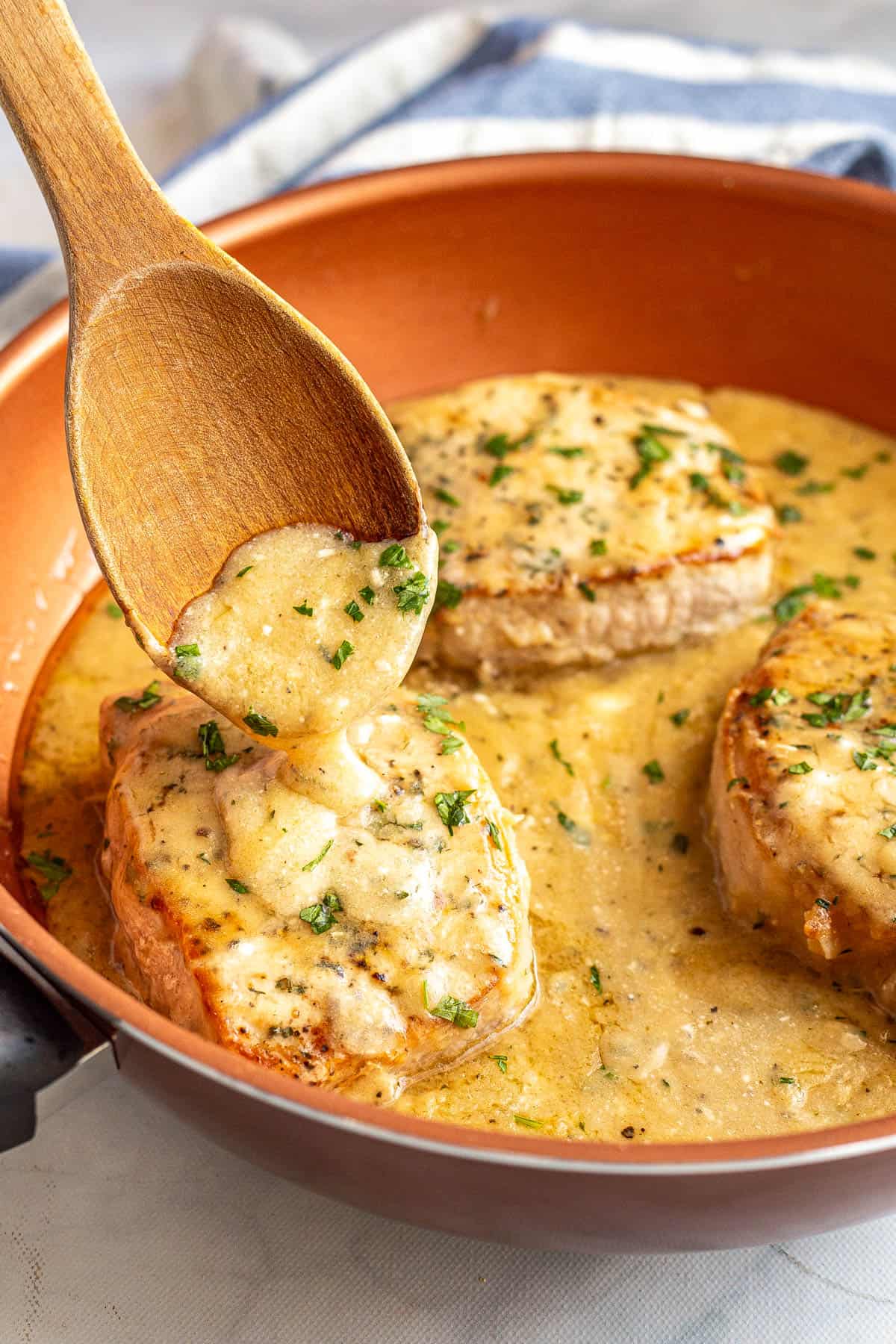 A wooden spoon drizzling pan gravy over seared pork chops in a copper pan.