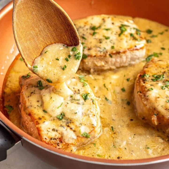 Close up of a wooden spoon drizzling pan gravy over seared pork chops.