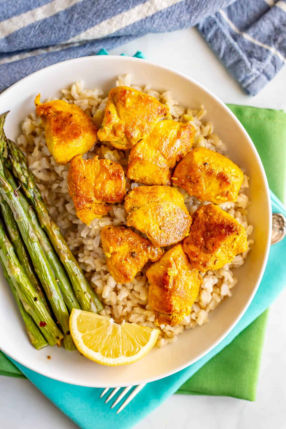 Turmeric chicken served over steamed brown rice alongside asparagus in a white low bowl.