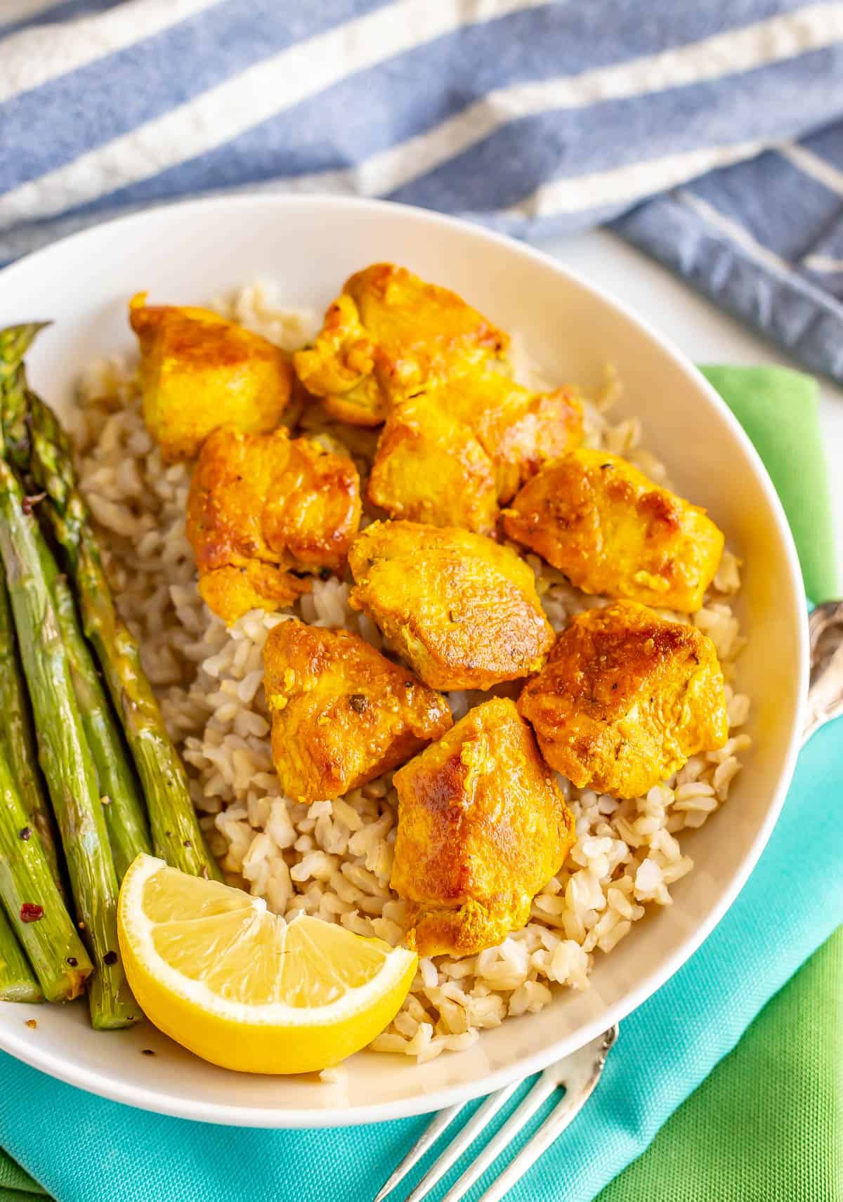 A dinner plate with asparagus, rice and seasoned chicken cubes with a lemon wedge on the side.