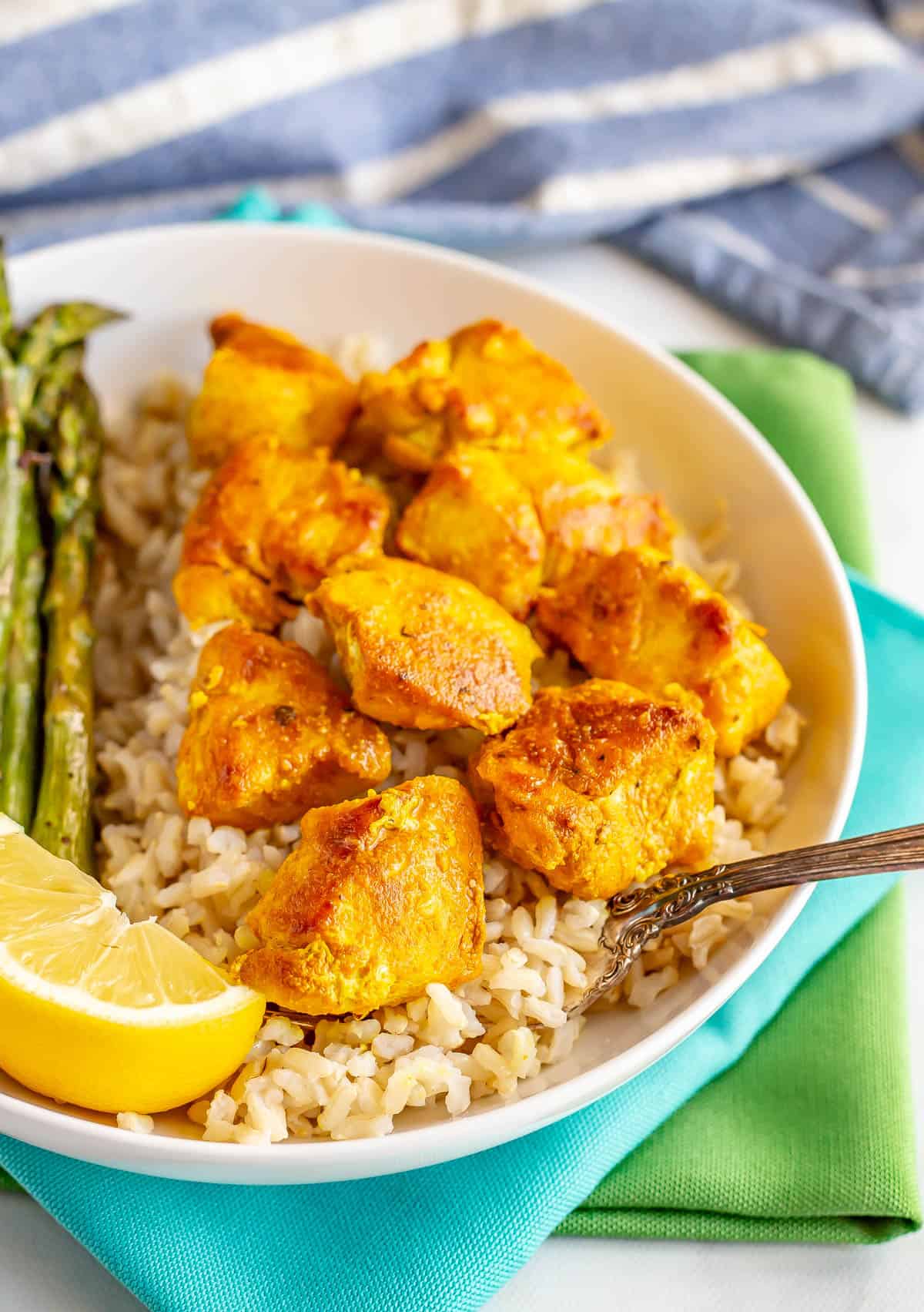 A fork resting in a bowl of chicken served over rice with a lemon wedge to the side.