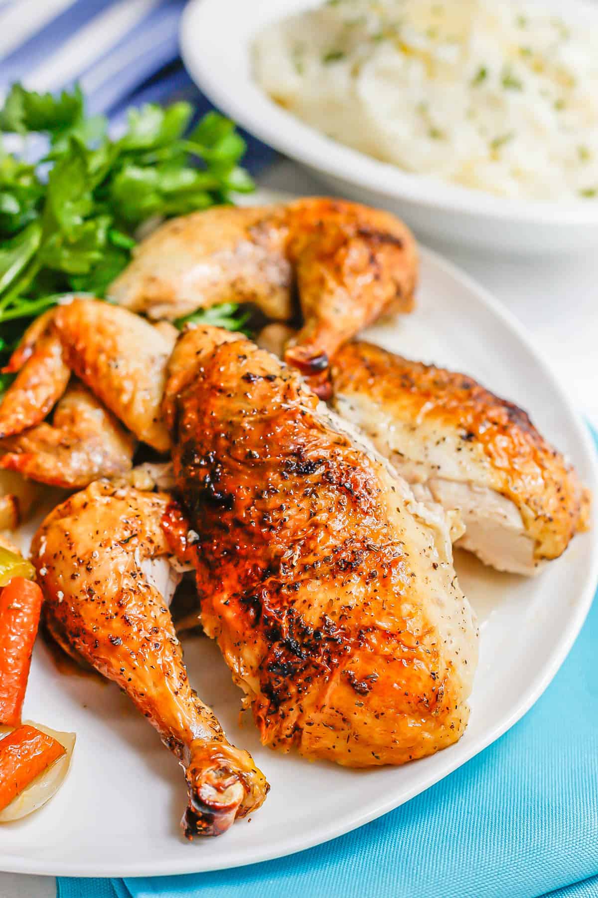 Close up of a whole roasted chicken broken down into parts and arranged on a white plate.