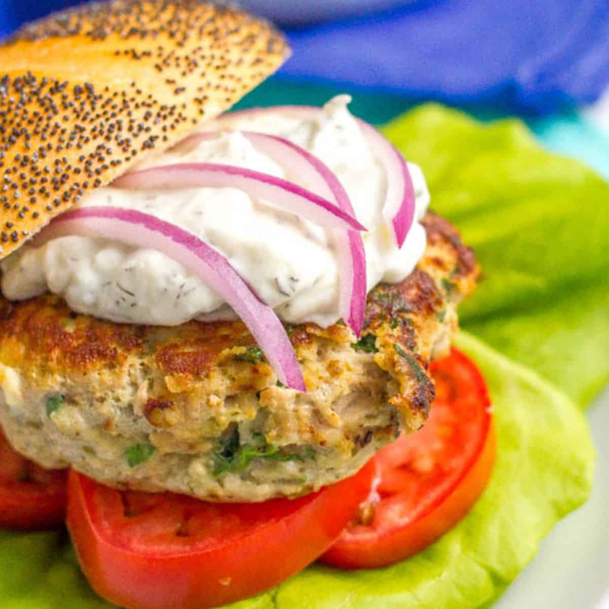 Close up of a Greek turkey burger with spinach mixed into the patty served on a bun with tzatziki sauce and sliced red onions.